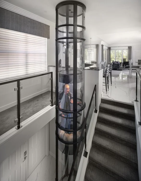 Pneumatic Vacuum Elevator Beside Staircase Person riding a two stop PVE pneumatic vacuum elevator with glass tube beside a staircase in an open plan home