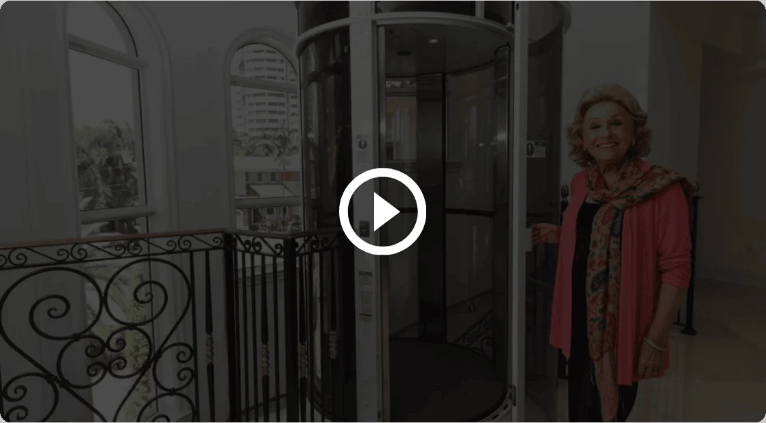 Home elevator video overlay Video play button over a woman standing beside a PVE home elevator with a glass tube